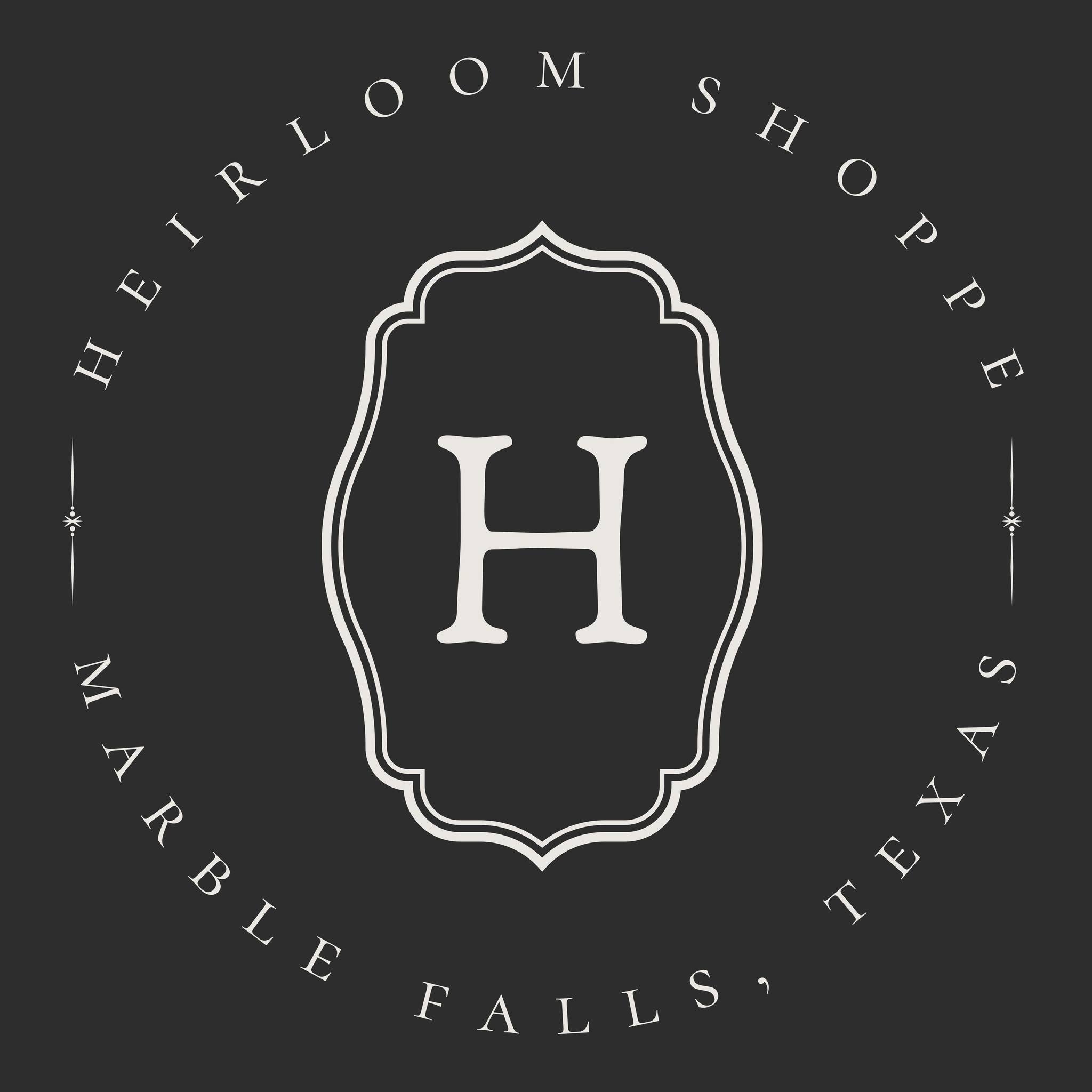 A black and white logo with a decorative frame around a large H. The text around the frame reads Heirloom Shoppe, Marble Falls, Texas—perfect for those seeking vintage decor and timeless heirloom gifts.