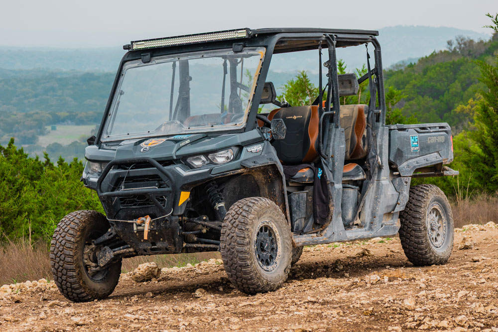 A rugged off-road utility vehicle with four seats, dusty tires, and a roll cage is parked on a dirt path at Hidden Falls Adventure Park, surrounded by greenery and hills in the background.