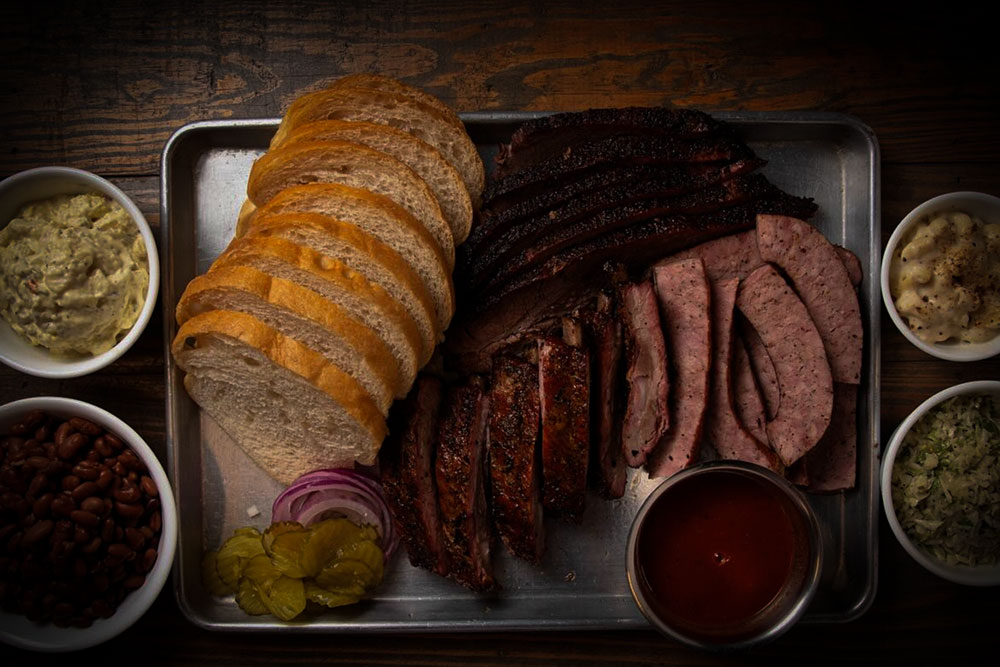 Perfect for a Guys Weekend in Burnet County, this tray features sliced white bread, brisket, ribs, sausage, pickles, red onion, and barbecue sauce. Surrounding sides include coleslaw, macaroni and cheese, baked beans, and potato salad.
