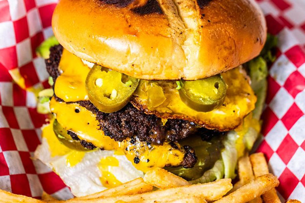 A cheeseburger topped with melted cheddar, jalapeño slices, lettuce, and pickles, served on a checkered red and white paper next to golden French fries—classic Burger at Old Oak Burger in Marble Falls.