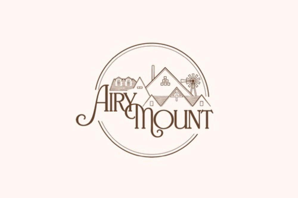 Logo for Airy Mount featuring stylized cursive text integrated with illustrations of house rooftops, a chimney, and a windmill—inviting you to plan a Girls Weekend or 3 Day Itinerary in scenic Burnet County—all enclosed within a circular border on a light background.