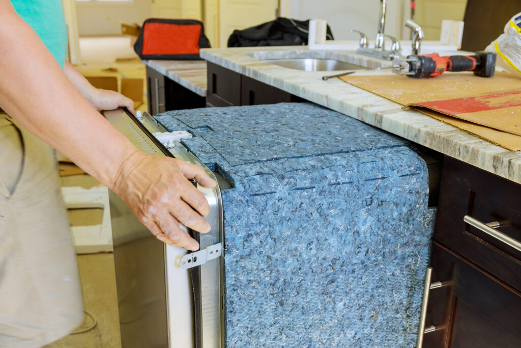 Professional Dishwasher Installation | Absolute Plumbing - Absolute Plumbing Plumber installing a new stainless steel dishwasher for Fixture Replacement in a modern Marble Falls, TX kitchen.