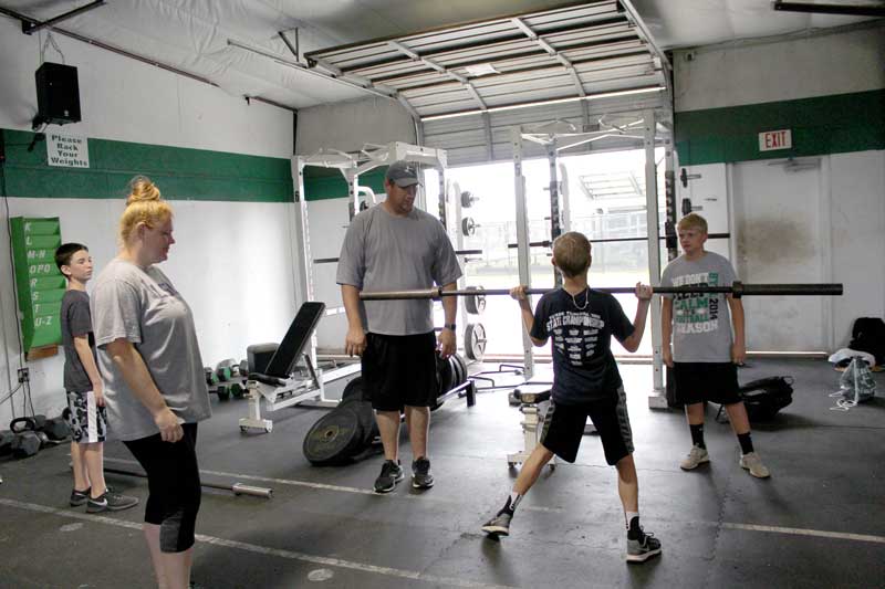 Burnet High School offensive line coach Eddy Parker demonstrates the proper way to perform a deadlift at the Burnet High School fieldhouse weight room for Grant Jones and Luke Hudgins (right) as his wife, Lacy Parker, a girls basketball and track coach, looks on. Staff photo by Jennifer Fierro