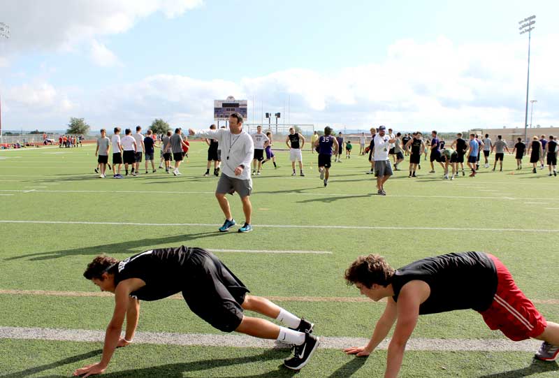 Marble Falls High School interim head football coach Mike Birdwell lines up players to perform mat drills as defensive coordinator Chad Bishop (back, left) encourages them during summer conditioning in June. Staff photo by Jennifer Fierro