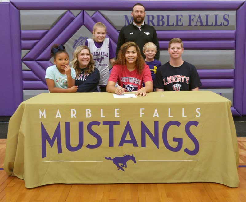 Marble Falls High School senior basketball player Mya McMillian (seated, center) signs her National Letter of Intent on Nov. 13 to play for Liberty University. She is surrounded by sister Aaliyah (seated, left), mother Lauren Berkman, sister Allyssa (standing), Marble Falls High School interim athletics director Mike Birdwell, brother Beckett, and father John Berkman, who is also the Lady Mustangs coordinator and head basketball coach. Staff photo by Jennifer Fierro