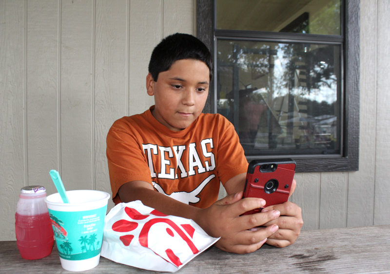 Marble Falls Middle School sixth-grader Nathan Jowers watches a video on his smartphone thanks to the new Wi-Fi service at Westside Park. Jowers connected to the free service Aug. 9 while attending Westside Connection, a festive gathering hosted by the city of Marble Falls’s Community Engagement Initiative. Staff photo by Jennifer Fierro