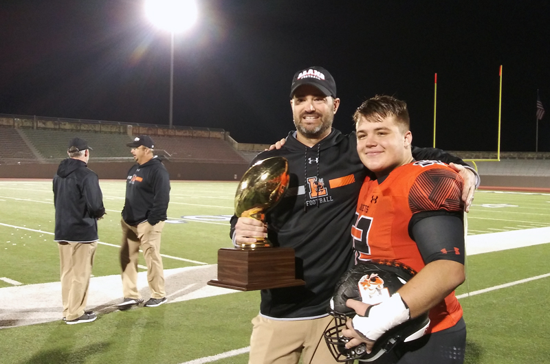 Llano High School head coach Matt Green and senior lineman Tyler Lindell with the bi-district championship trophy after the Yellow Jackets defeated Hondo 21-14 in overtime Nov. 16. Llano now faces Corpus Christi West Oso. The game kicks off at 1 p.m. Friday, Nov. 23, at Alamo Stadium, 760 Stadium Drive in San Antonio. Staff photo by Jennifer Fierro